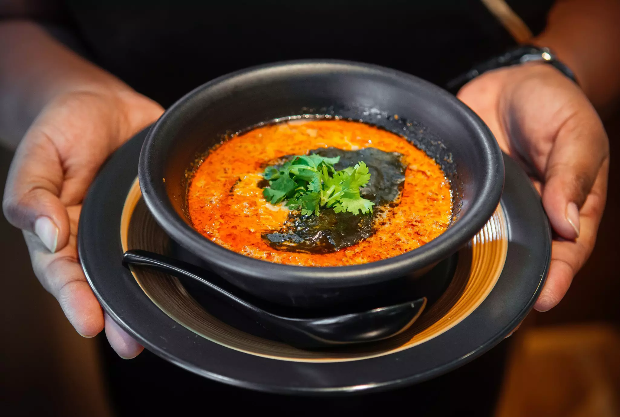 Waiter holds Peranakan dish ayam buah keluak (nut chicken stew curry) in a bowl
