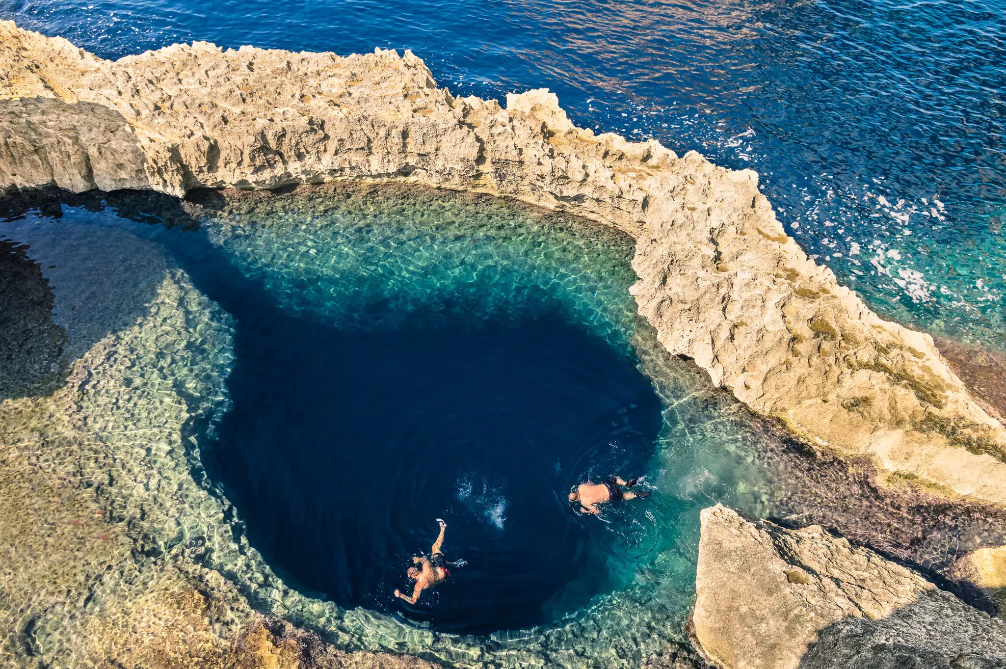 An overhead view of snorkelers at a blue swimming hole surrounded by rocky ledges