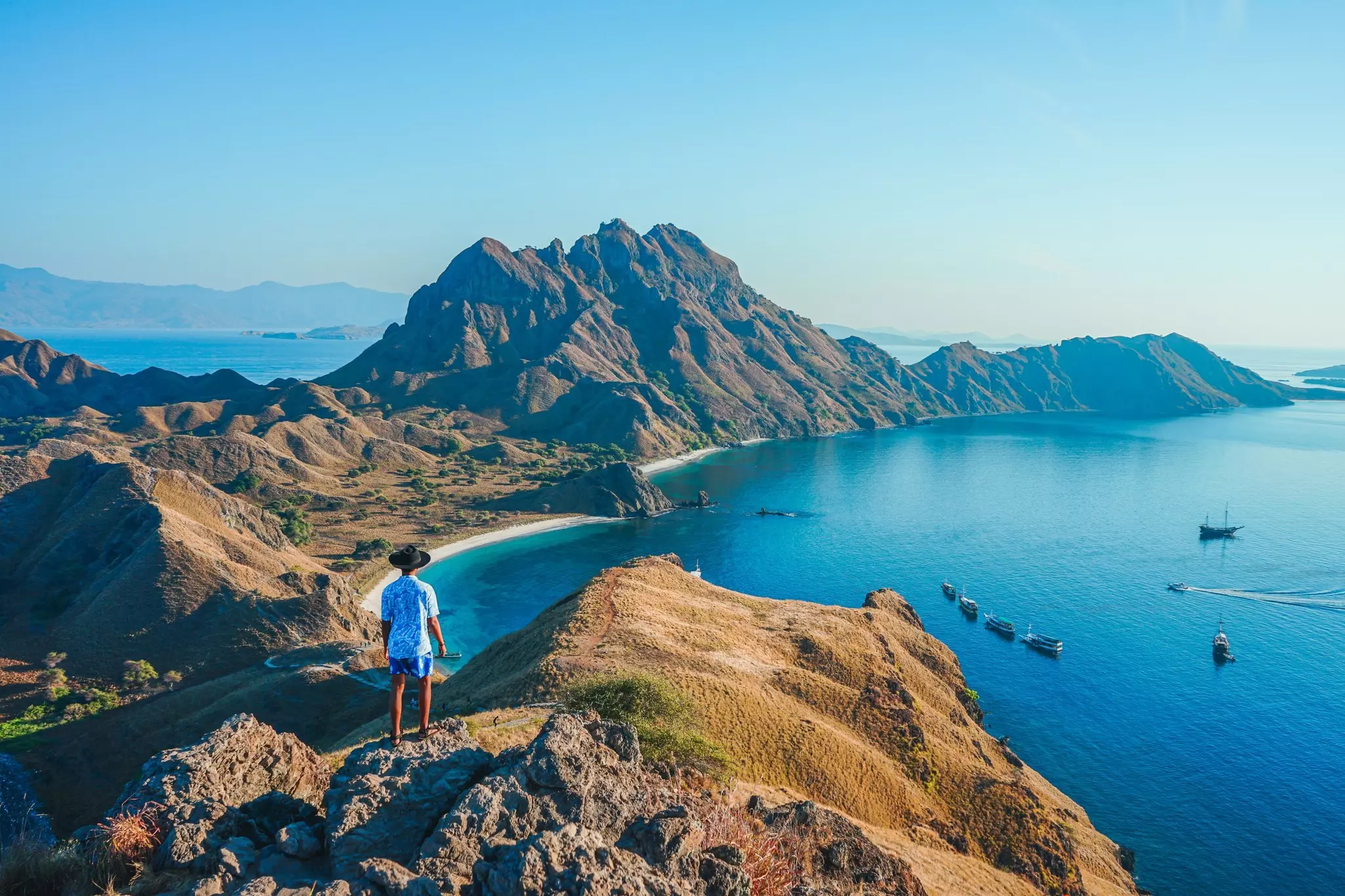 A man stands at a viewpoint looking down at the coastline of a mountainous island.
