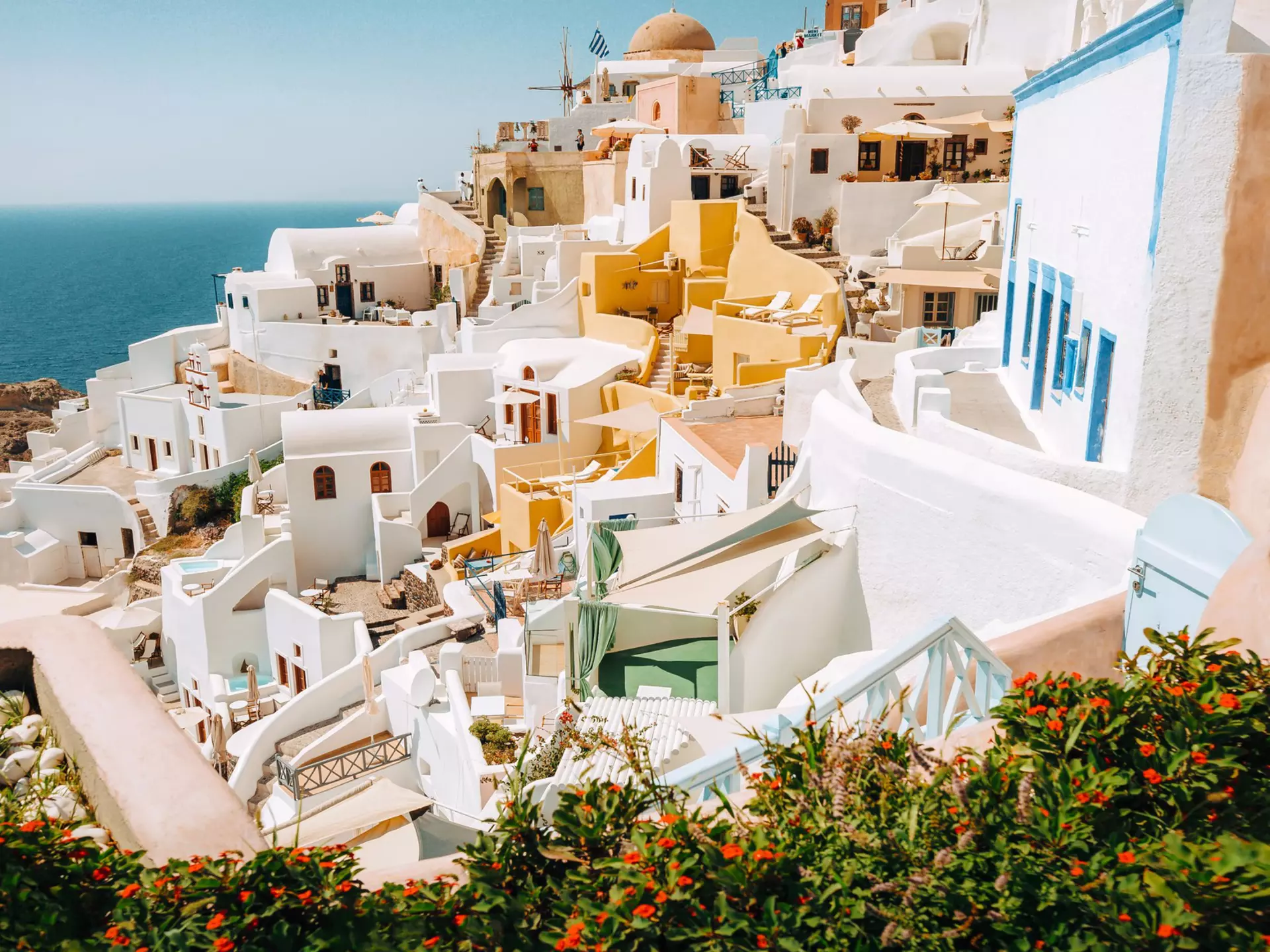  Picturesque view of traditional white-washed Santorini houses on small streets with flowers in foreground.