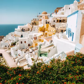  Picturesque view of traditional white-washed Santorini houses on small streets with flowers in foreground.