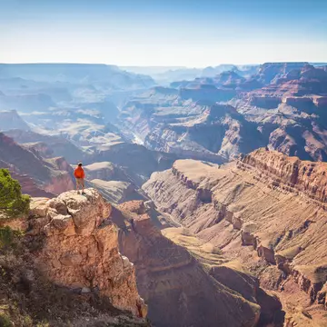 A male hiker is standing on a steep cliff taking in the amazing view over famous Grand Canyon on a beautiful sunny day with blue sky in summer, Grand Canyon National Park, Arizona, USA