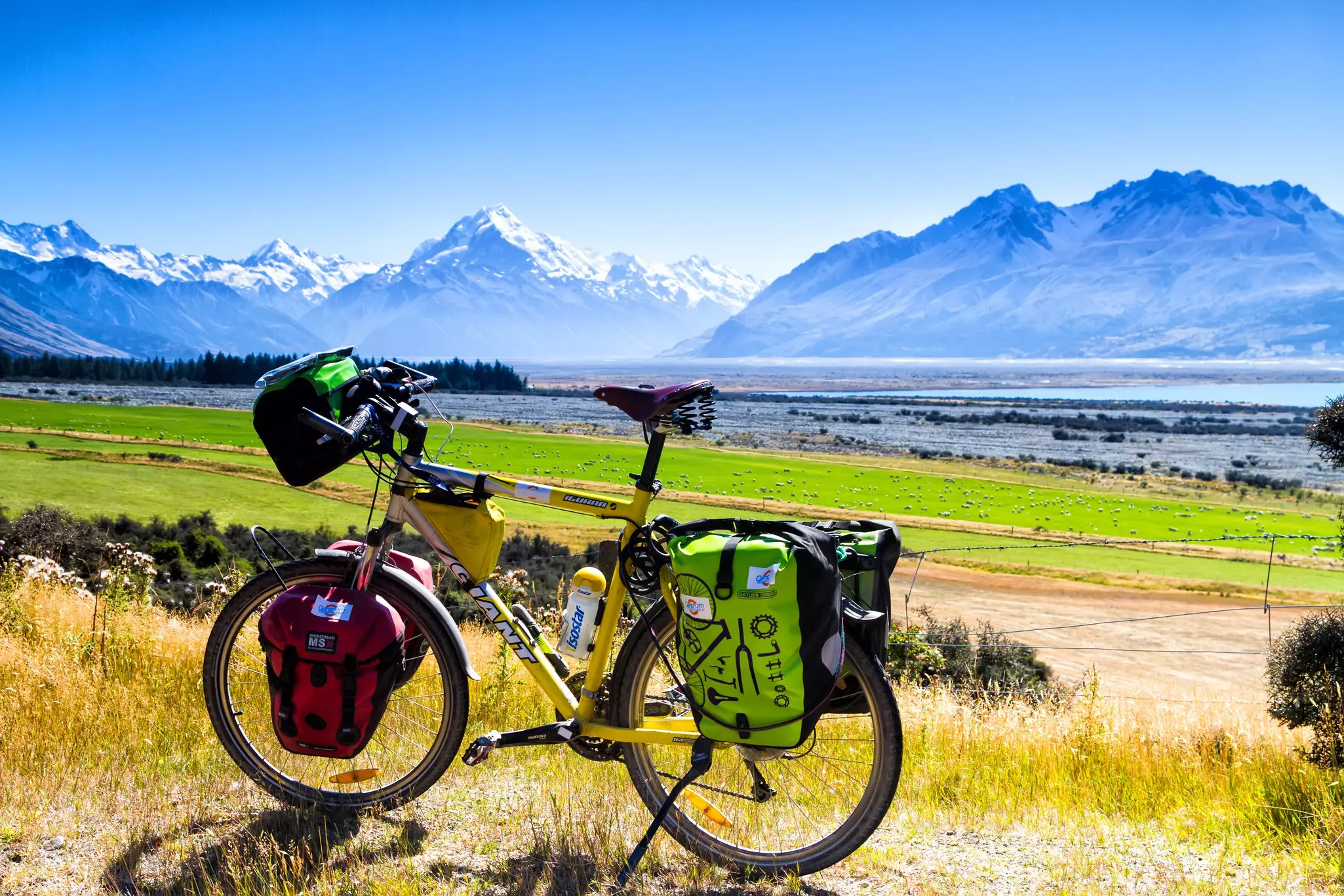 A yellow bike with loaded panniers in front of a snowy mountain range.