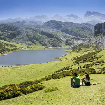 Young couple sitting on the grass overlooking the lakes in a mountainous region