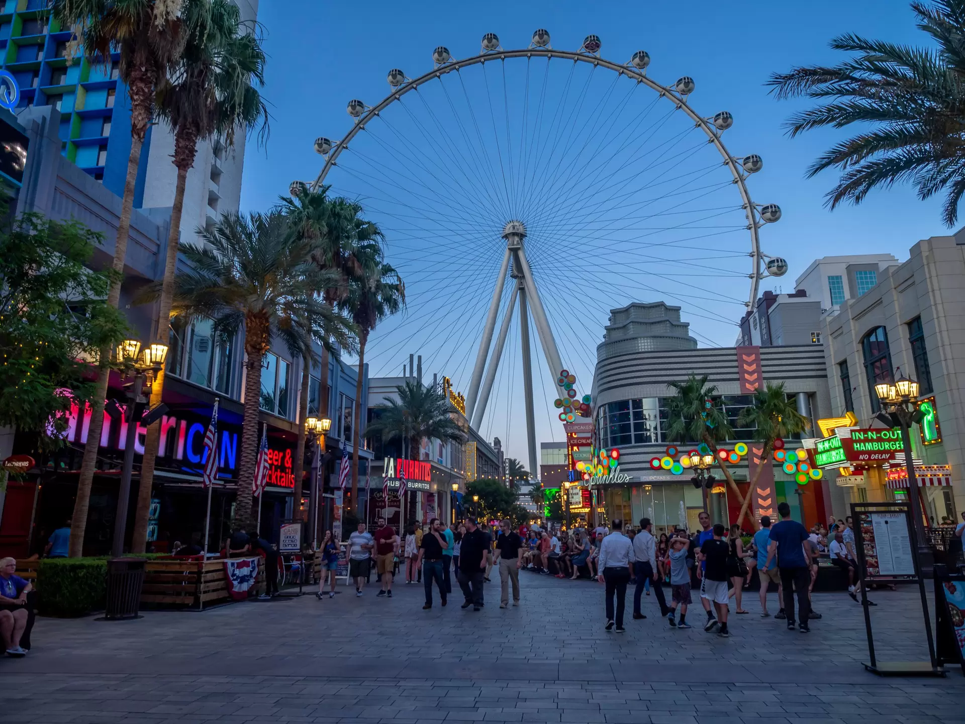 Sunset view of a promendade with a ferris wheel between high rise hotels in Las Vegas, Nevada.