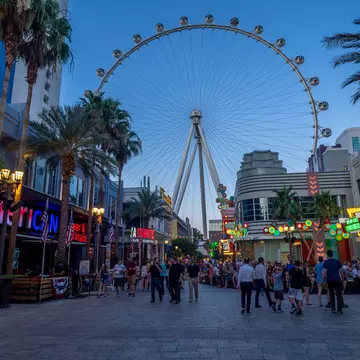 A giant observation wheel above a busy promenade lined with palms.