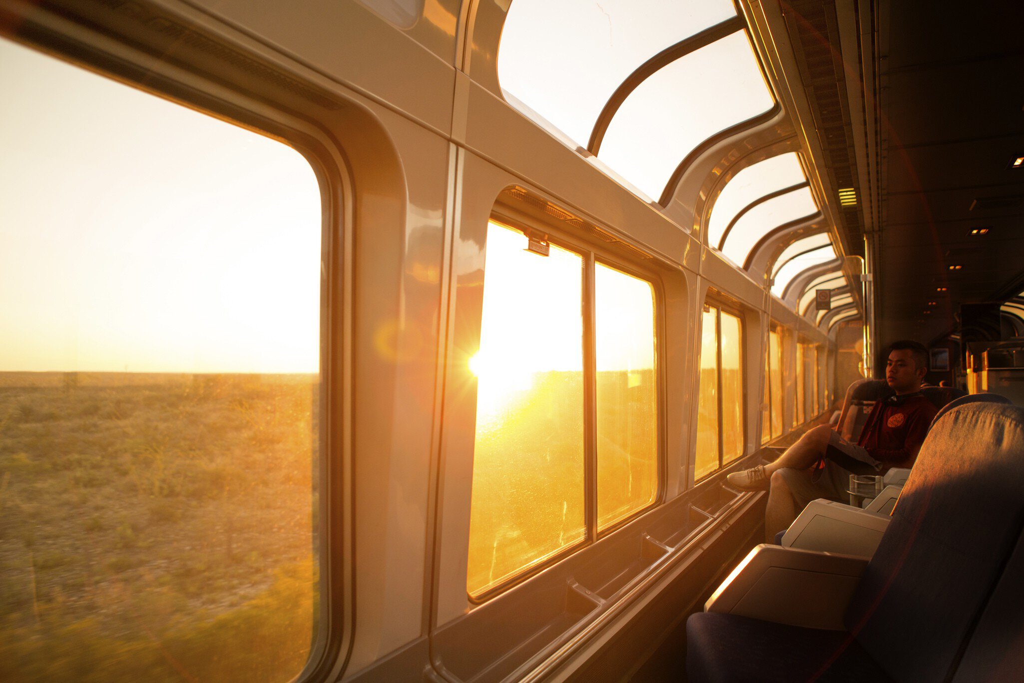 A passenger watches the sunrise from a train with large clear windows.