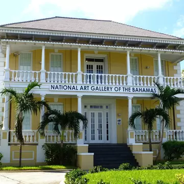A yellow colonial mansion with white columned verandas on two levels, fronted by palms and a lawn