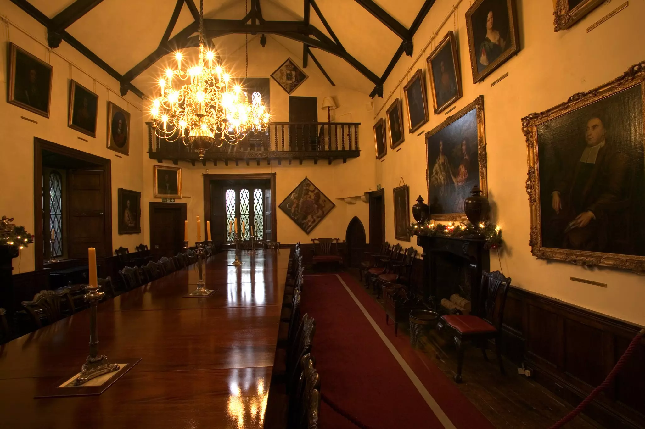 Room with a long, polished dark wood dining table lined with chairs. A chandelier hangs above it, and large painted portraits line the walls.