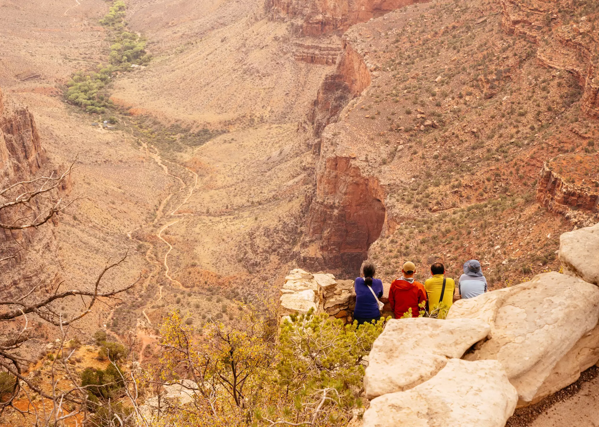 Hikers in colored coats sit on the rocky canyon rim in Grand Canyon National Park, USA.