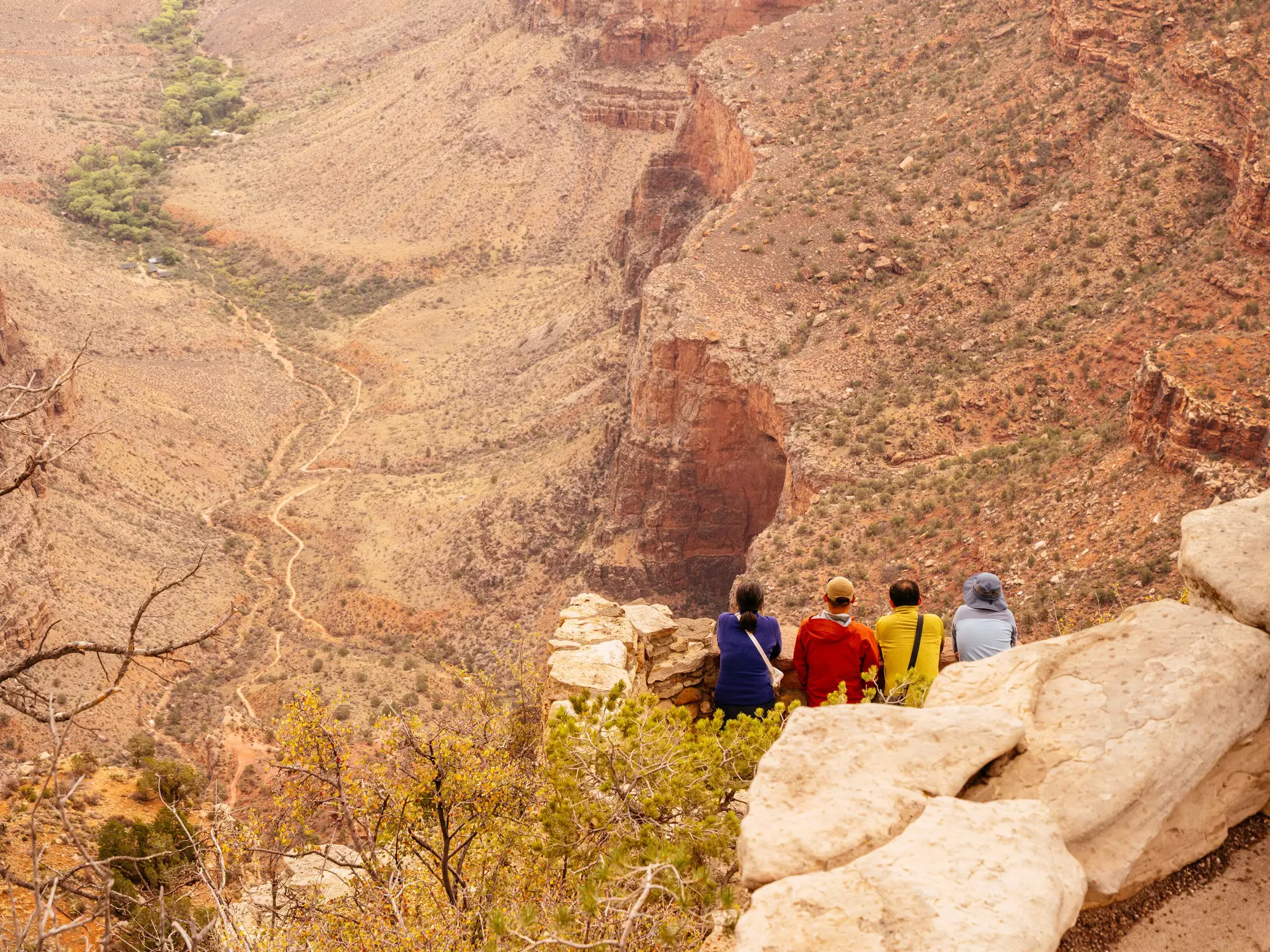 Hikers in colored coats sit on the rocky canyon rim in Grand Canyon National Park, USA.