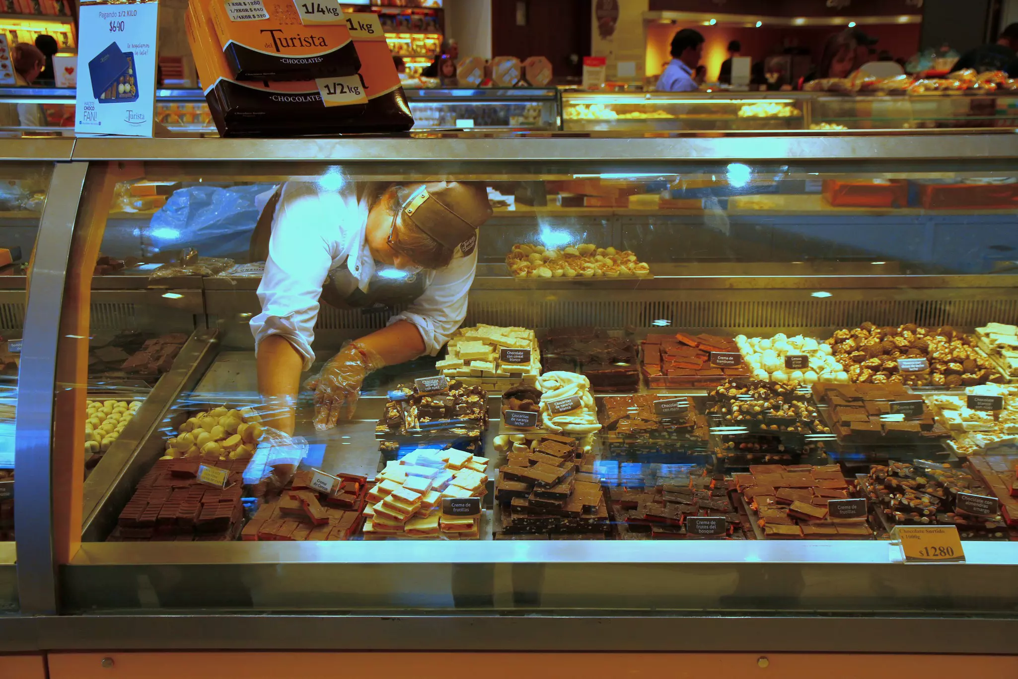 A worker reaches into a display case with many types of chocolate candy.