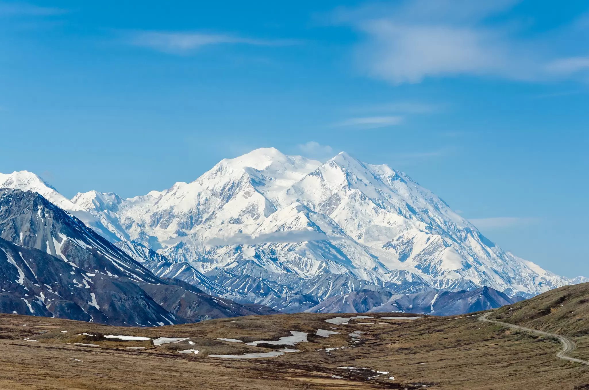 Snow-covered Denali rising above brown tundra and a winding park road in Alaska