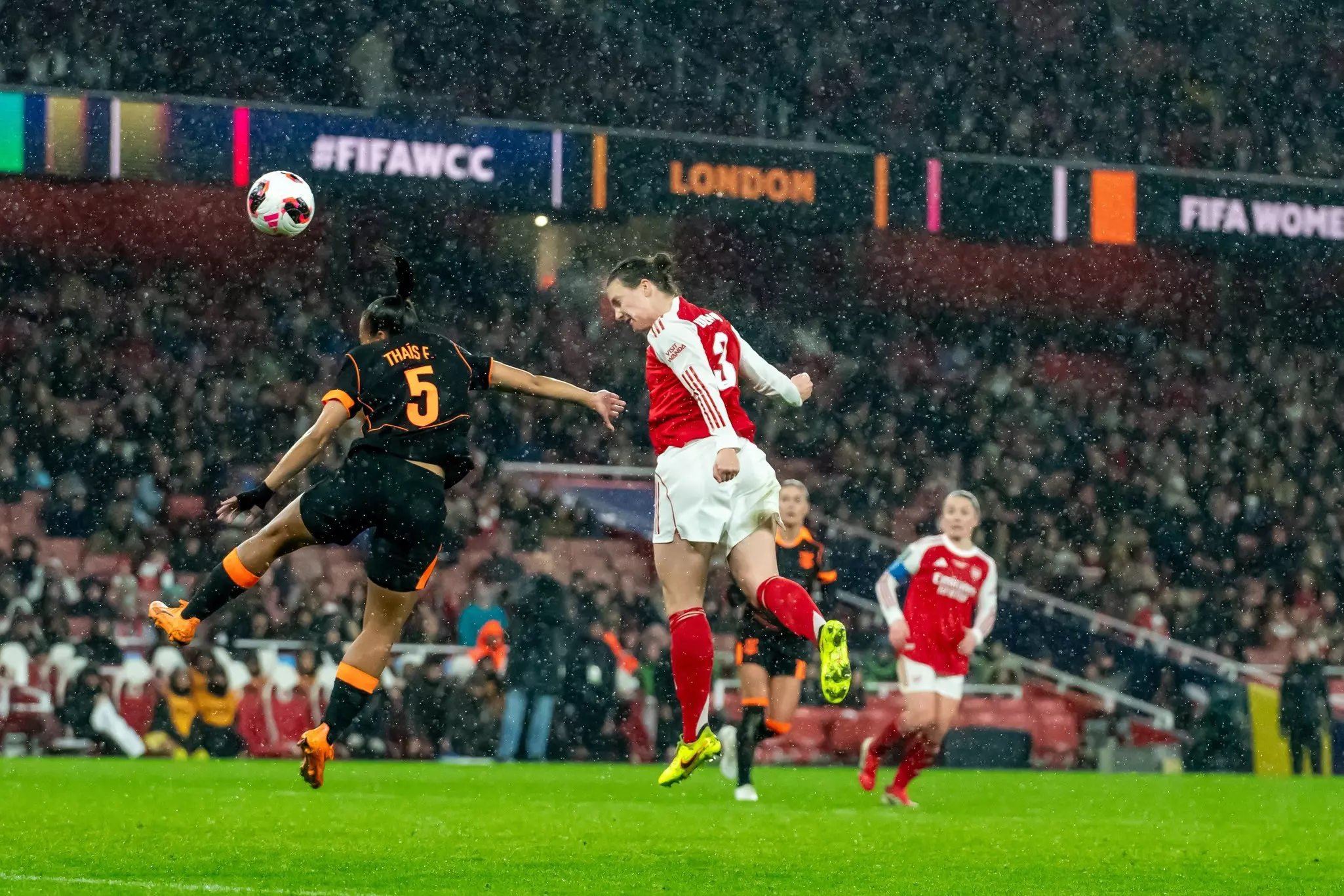 A woman heads a football during a match being played in a stadium in the pouring rain 
