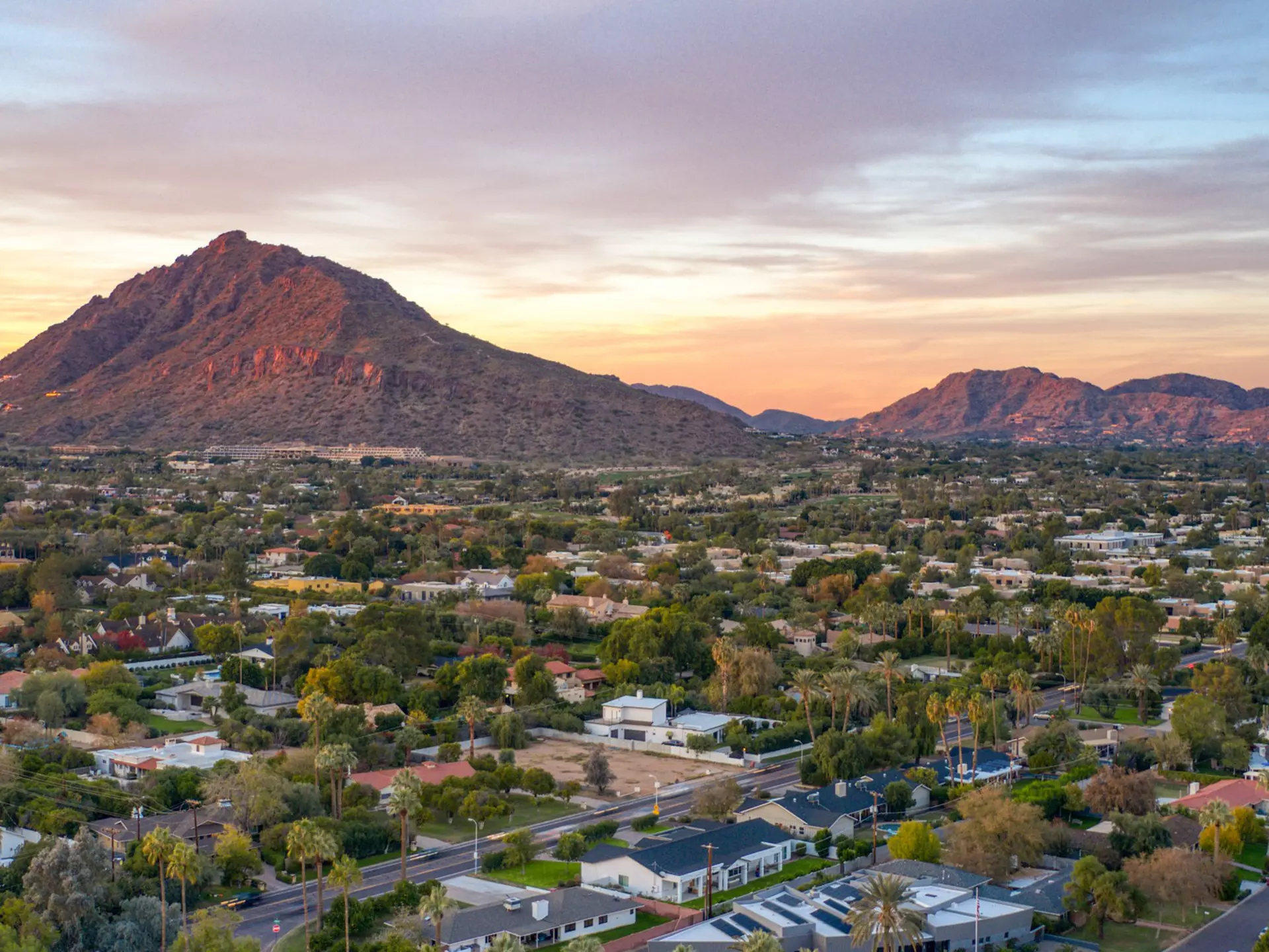 Sunset over Camelback Mountain, with a view of houses and trees in the foreground