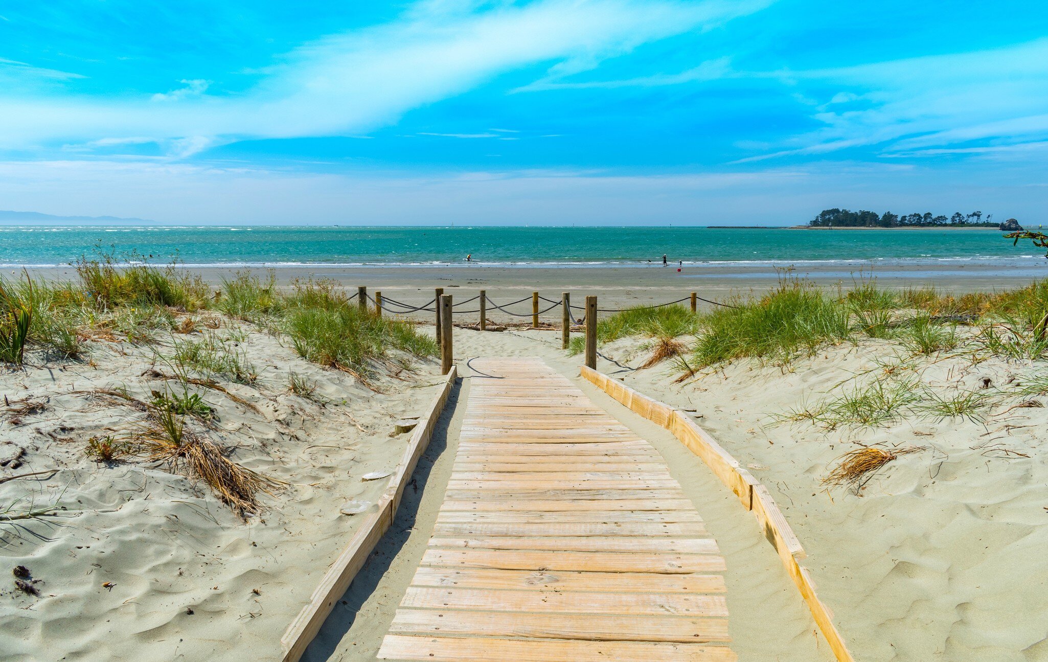 View of a wooden trail leading to Tāhunanui Beach on a sunny day in Nelson, New Zealand.