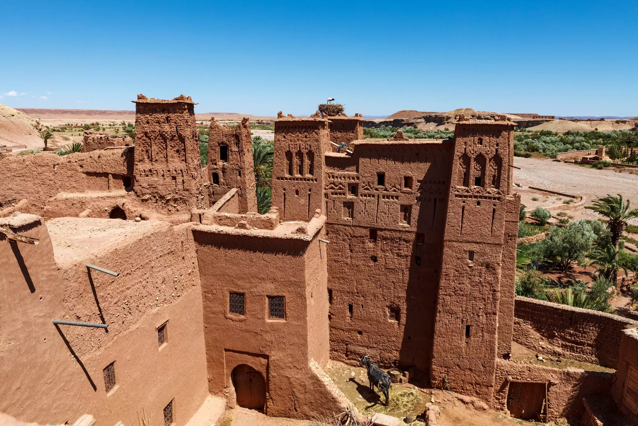 Aerial view of a brown building with towers and greenery in background