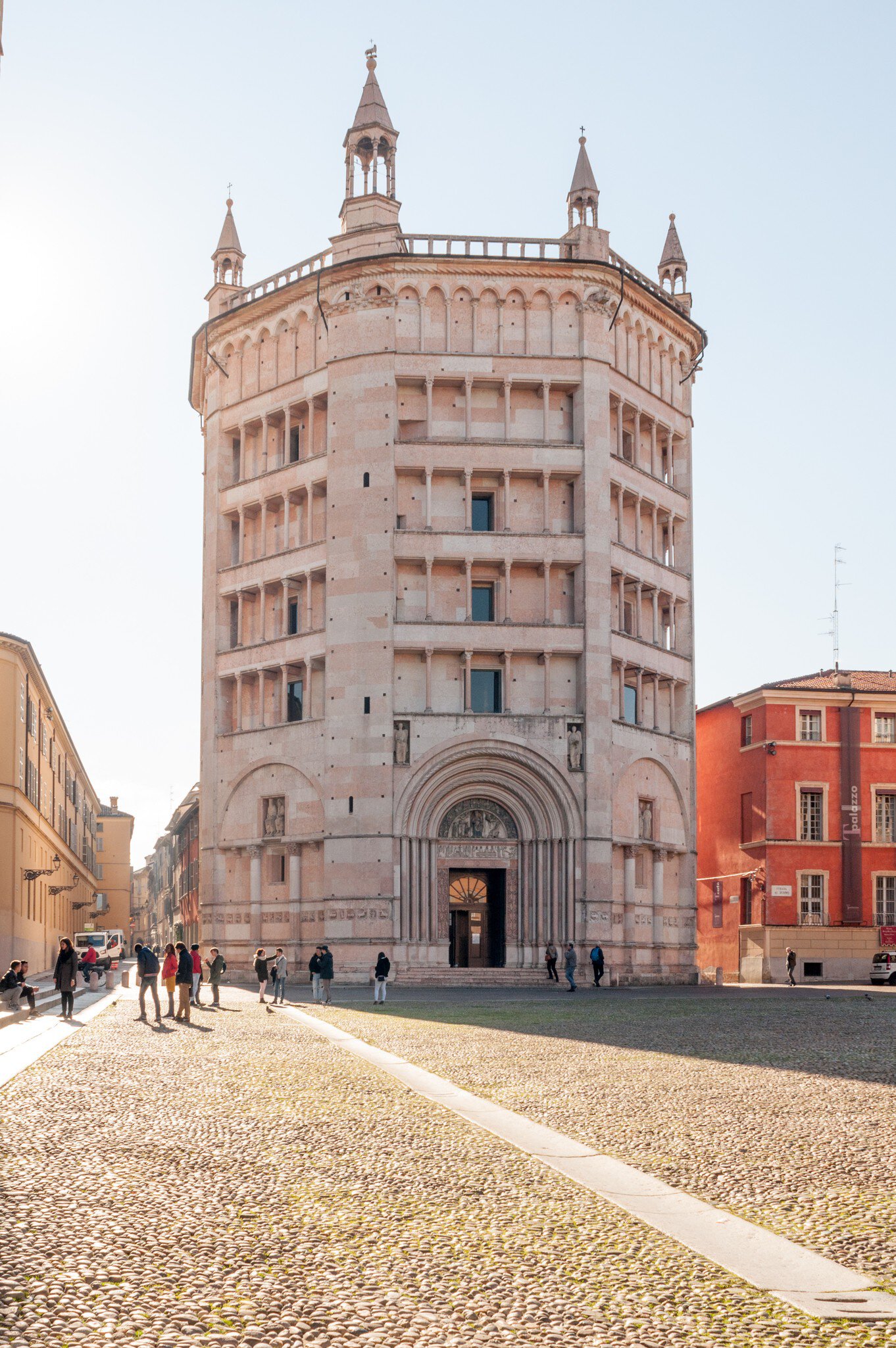 A view of the baptistery of Parma in Duomo square (Piazza Duomo) while tourists walk nearby.