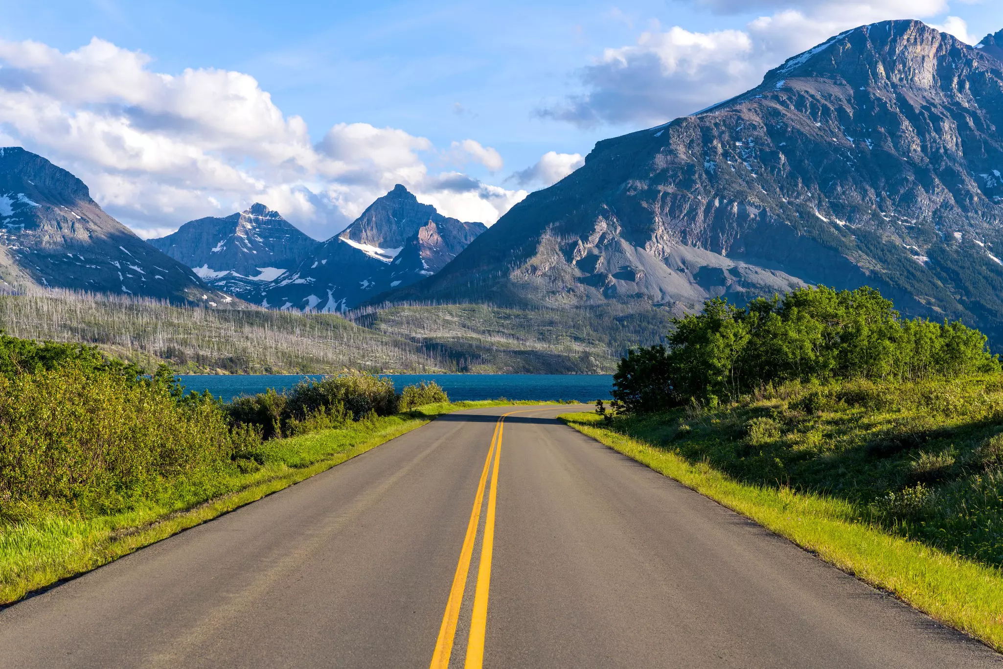 A road in a mountainous area descends towards a lake
