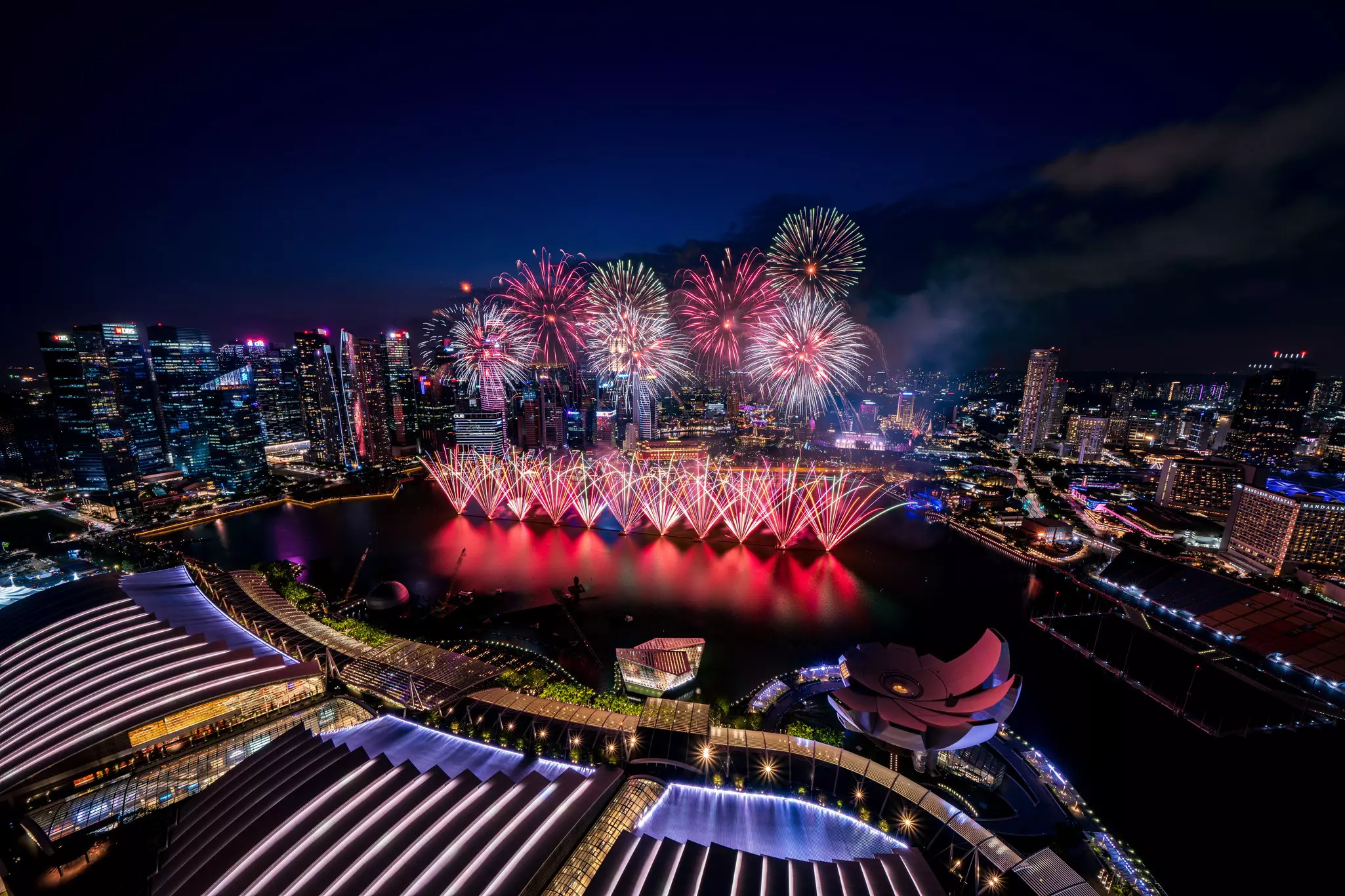 An aerial view of spectacular fireworks exploding over a harbor in a city.