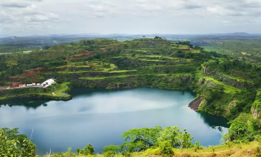 Liberia: flooded former mine pit lake surrounded by terraced, forested slopes under a cloudy sky