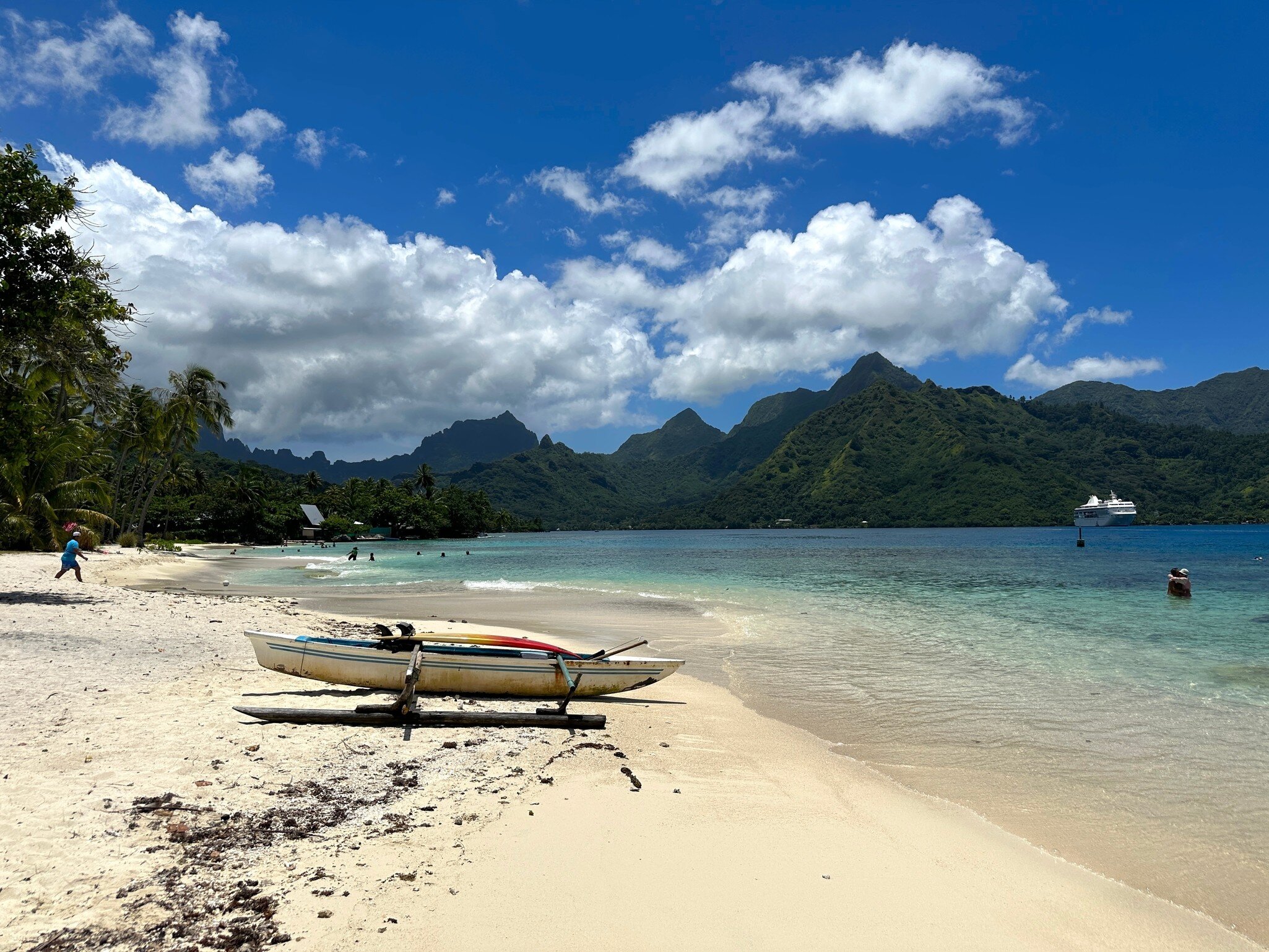 Outrigger canoe on white sand at Taʻahiamanu Beach, with turquoise water and green peaks of Mo'orea behind.