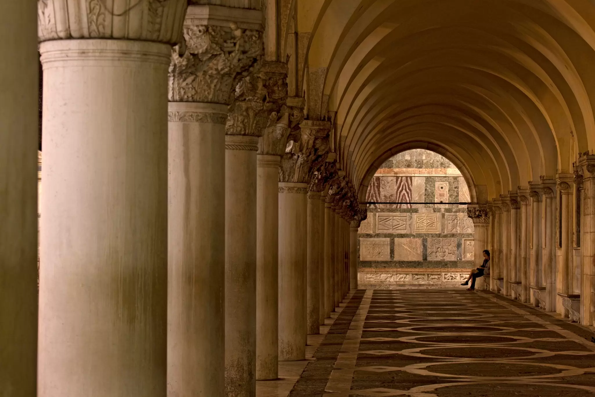 A woman sitting under the arches of Palazzo Ducale in Venice, Italy.