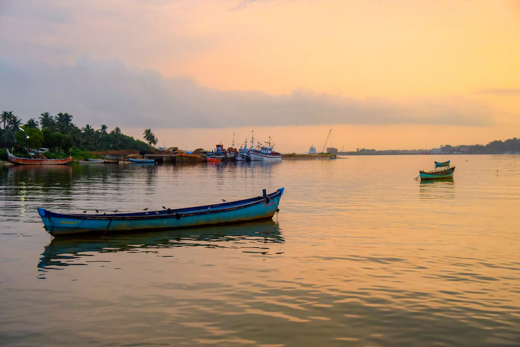 A small blue boat on a river at sunset; other boats are in the background.