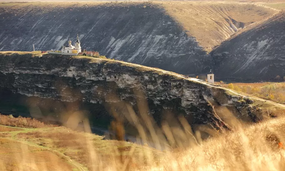 Orheiul Vechi, Moldova: monastery church and bell tower on a limestone cliff above a river gorge, golden grass in front