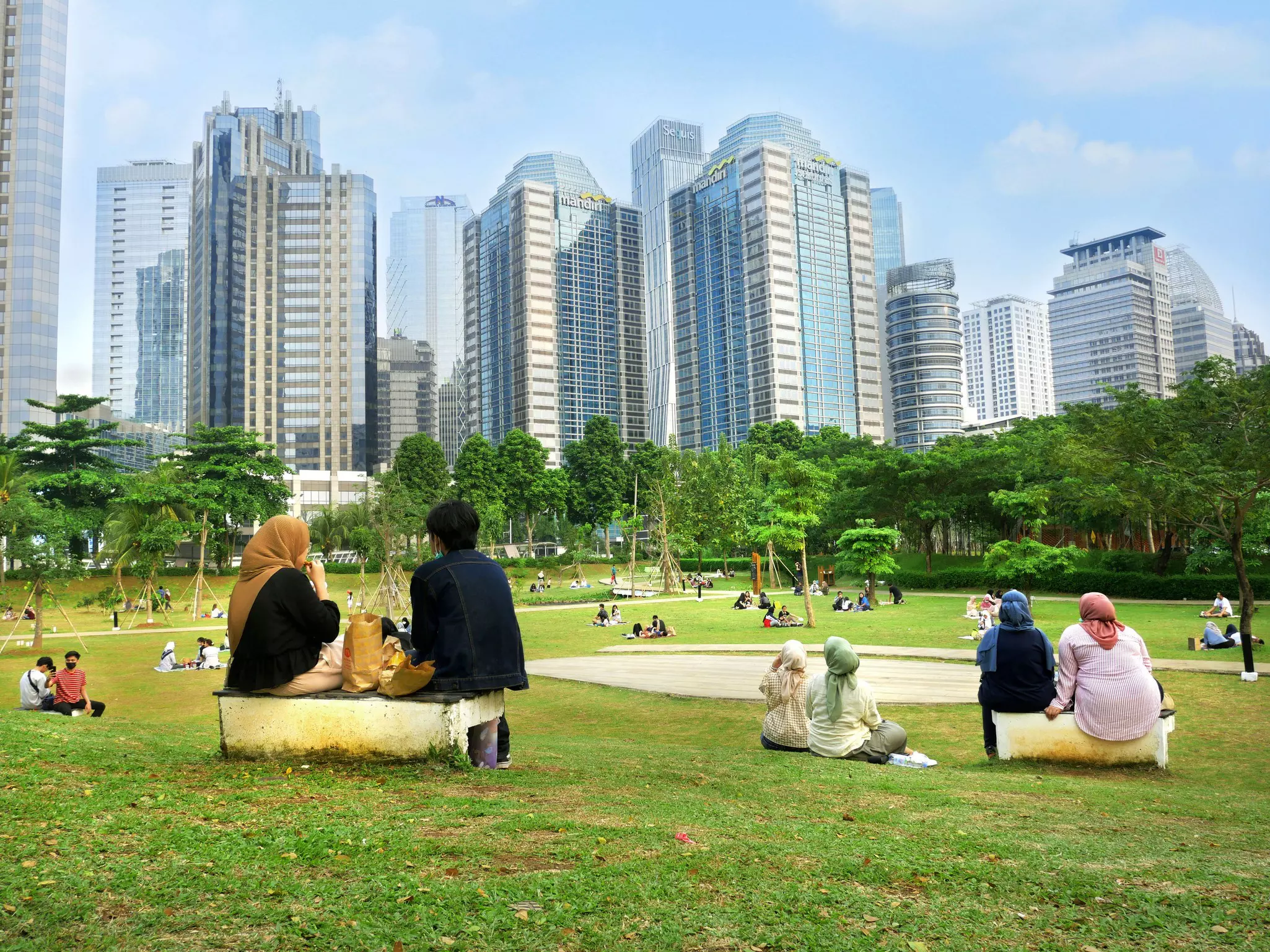 People sat in a green space within the high rise neighborhood of a city
