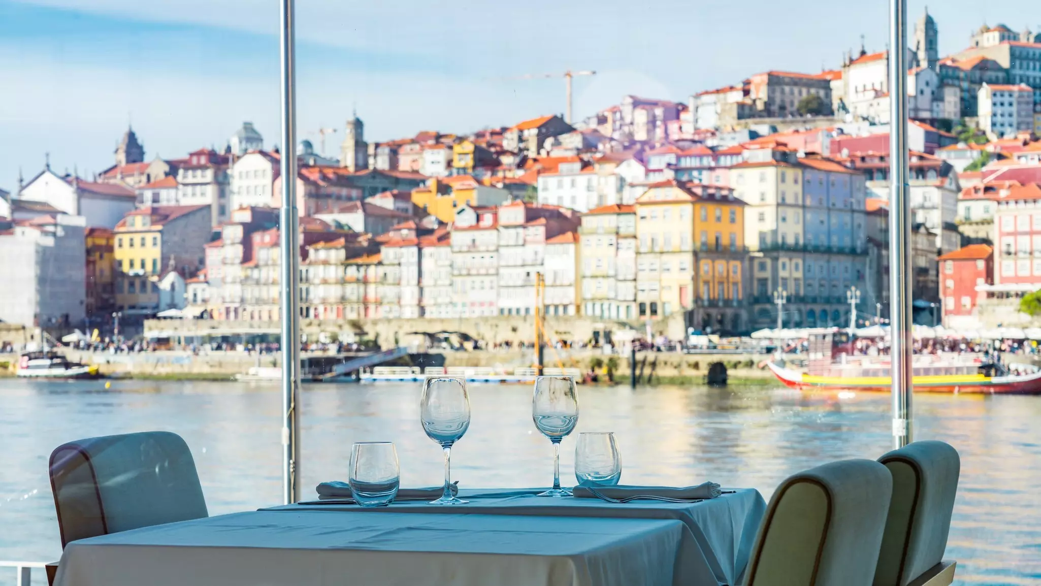 A table laid for lunch in a riverside restaurant with views of the pastel-colored buildings on the opposite side of the river.