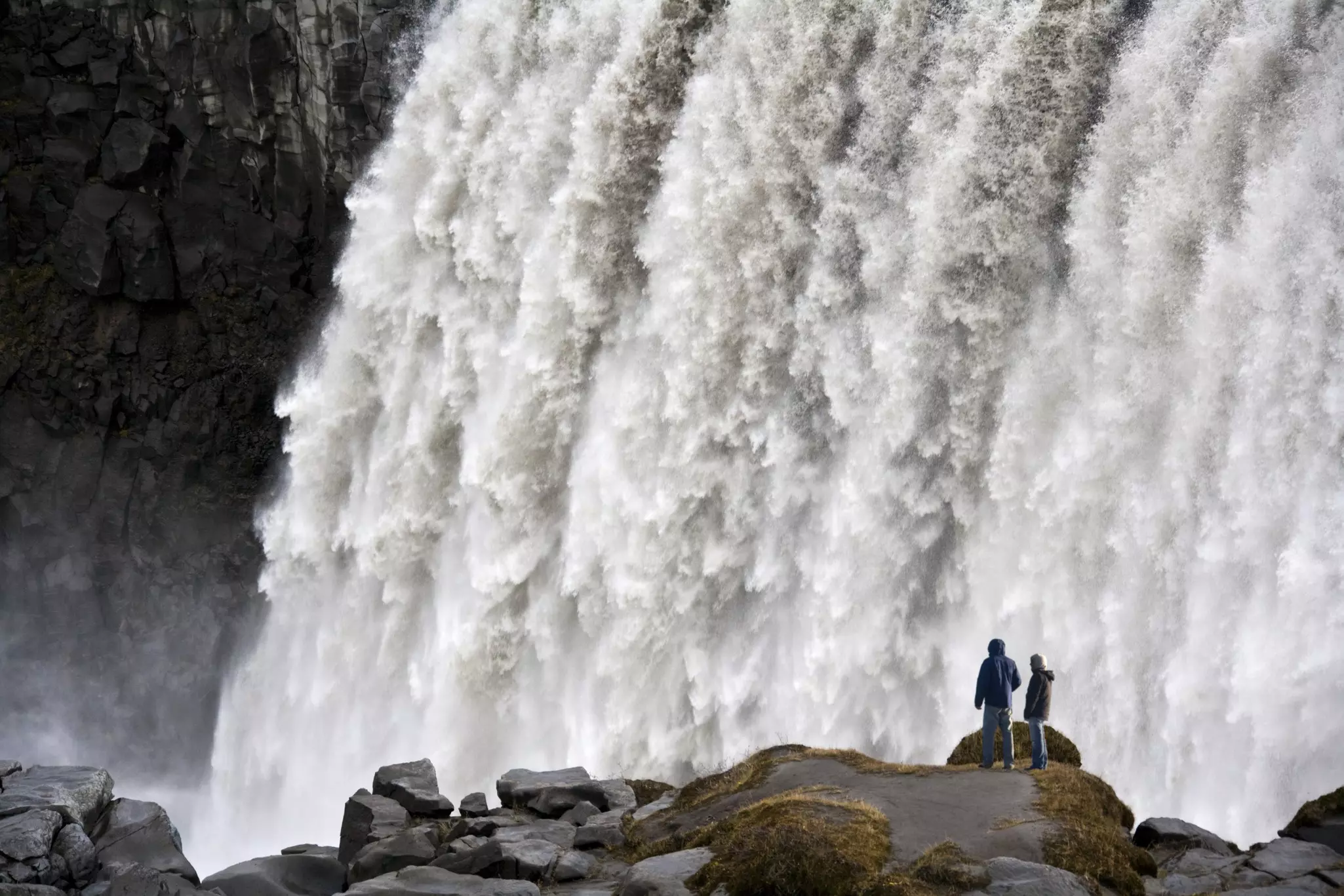 Two people are silhouetted in front of a powerful waterful.