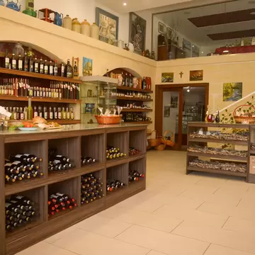 Wooden counter racked with wine bottles below arched stone shelves of bottles and jars, a staircase behind