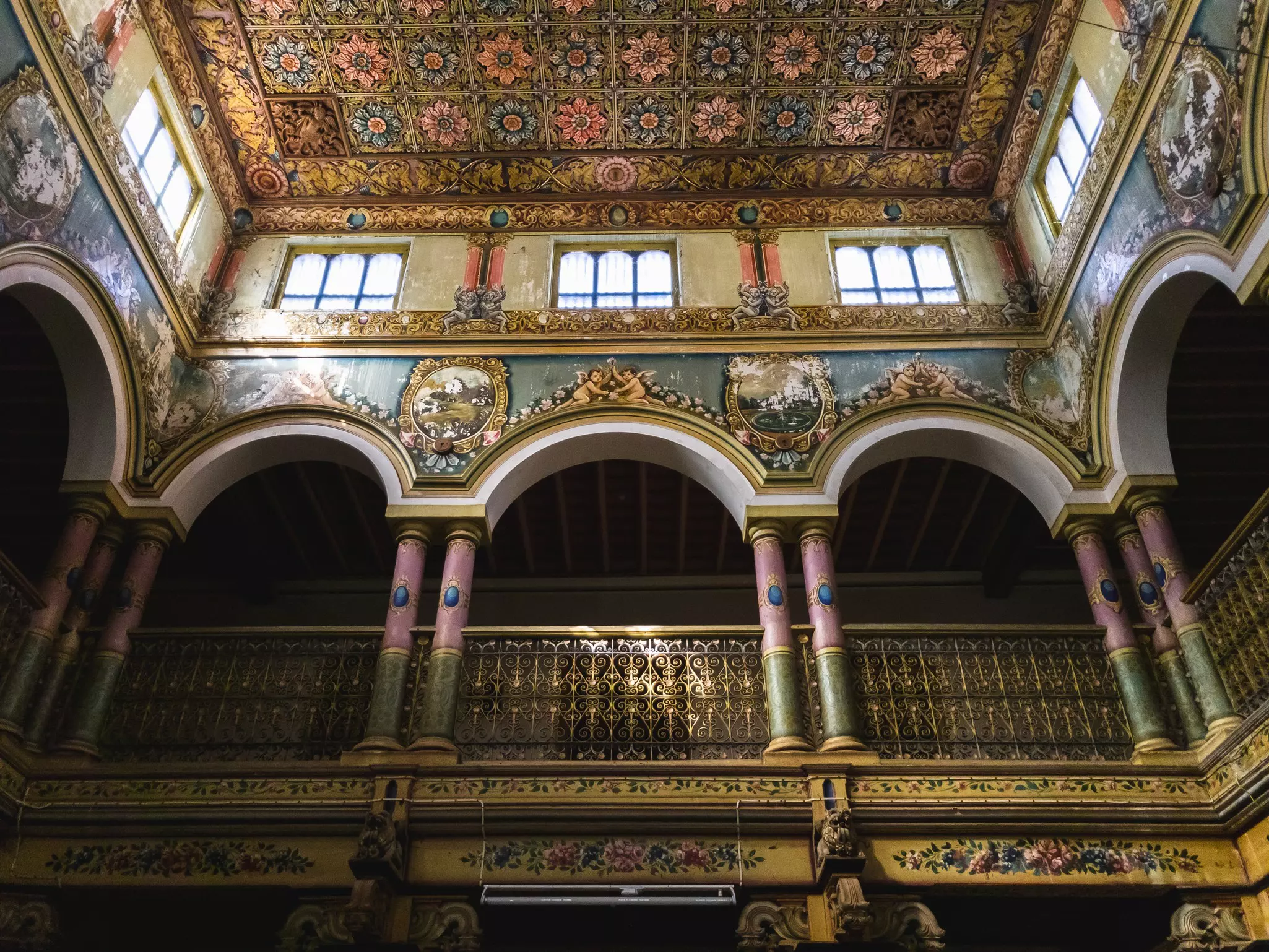 The opulent interior of a mansion has gilded columns, painted paster ornamentation and a coffered ceiling.