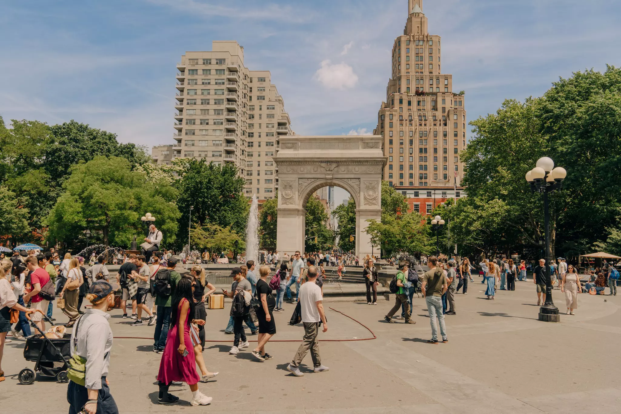 People walking around a busy park on sunny day with city views behind them.