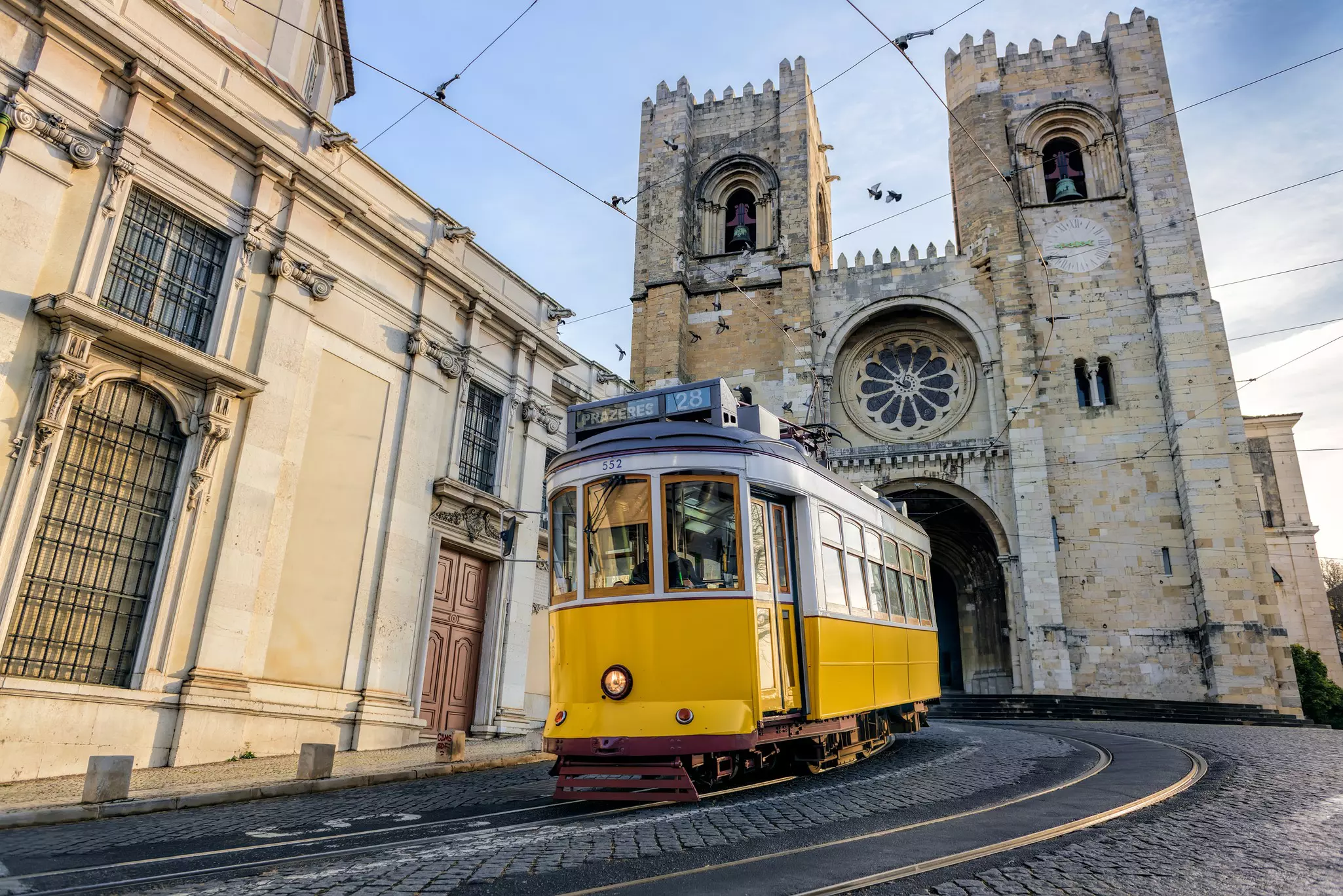 Yellow tram coming around a curve on cobblestone street with historic stone cathedral in the background.