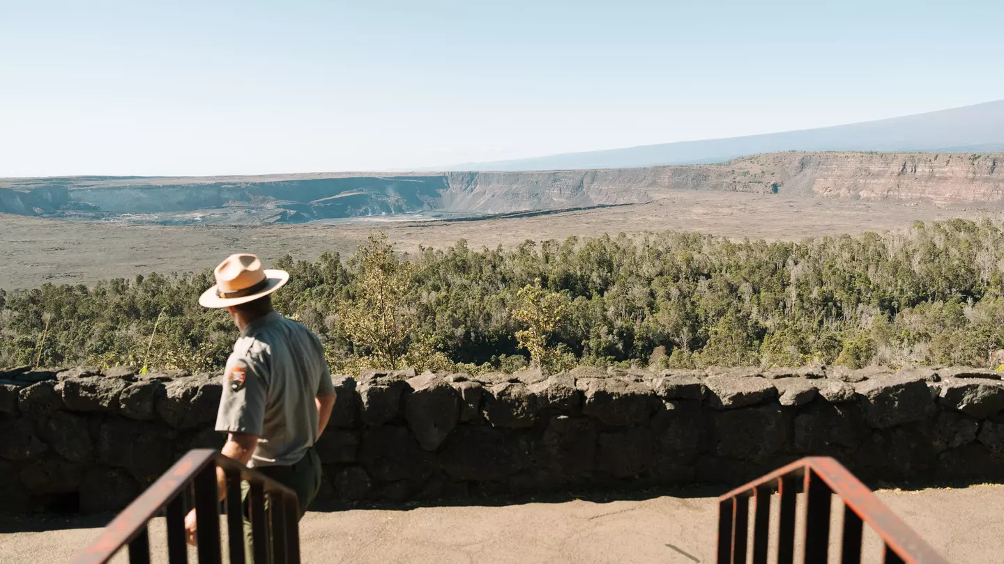 A park ranger looks out at a calder and low, flat hillside on an overcast day.