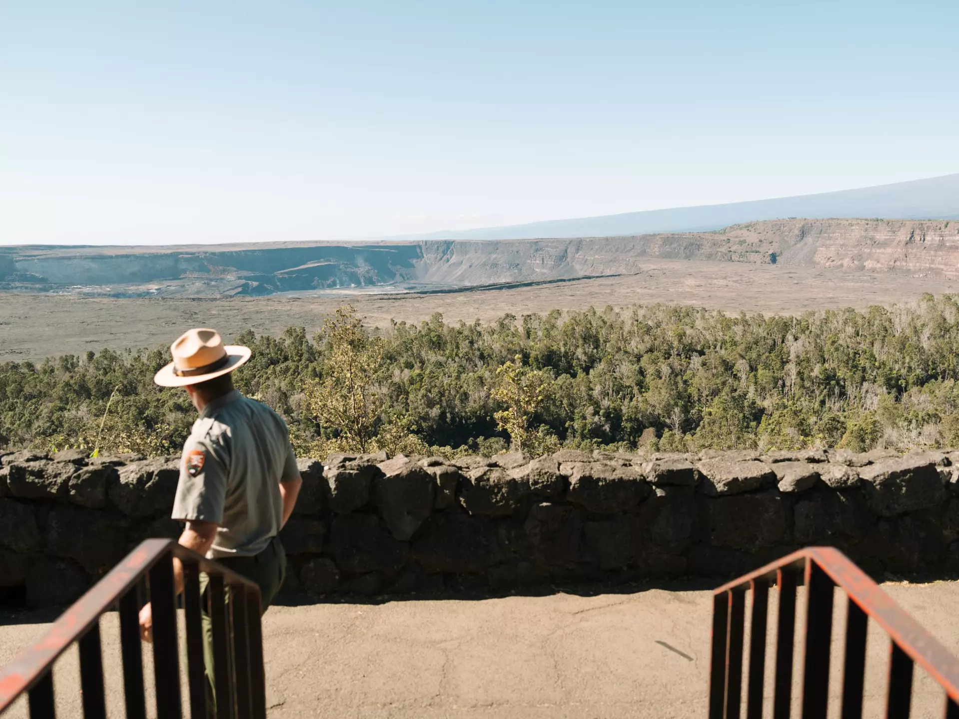 A park ranger looks out at a calder and low, flat hillside on an overcast day.