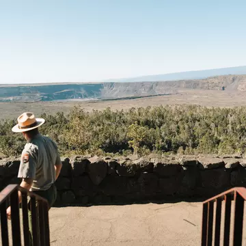 A park ranger looks out at a calder and low, flat hillside on an overcast day.