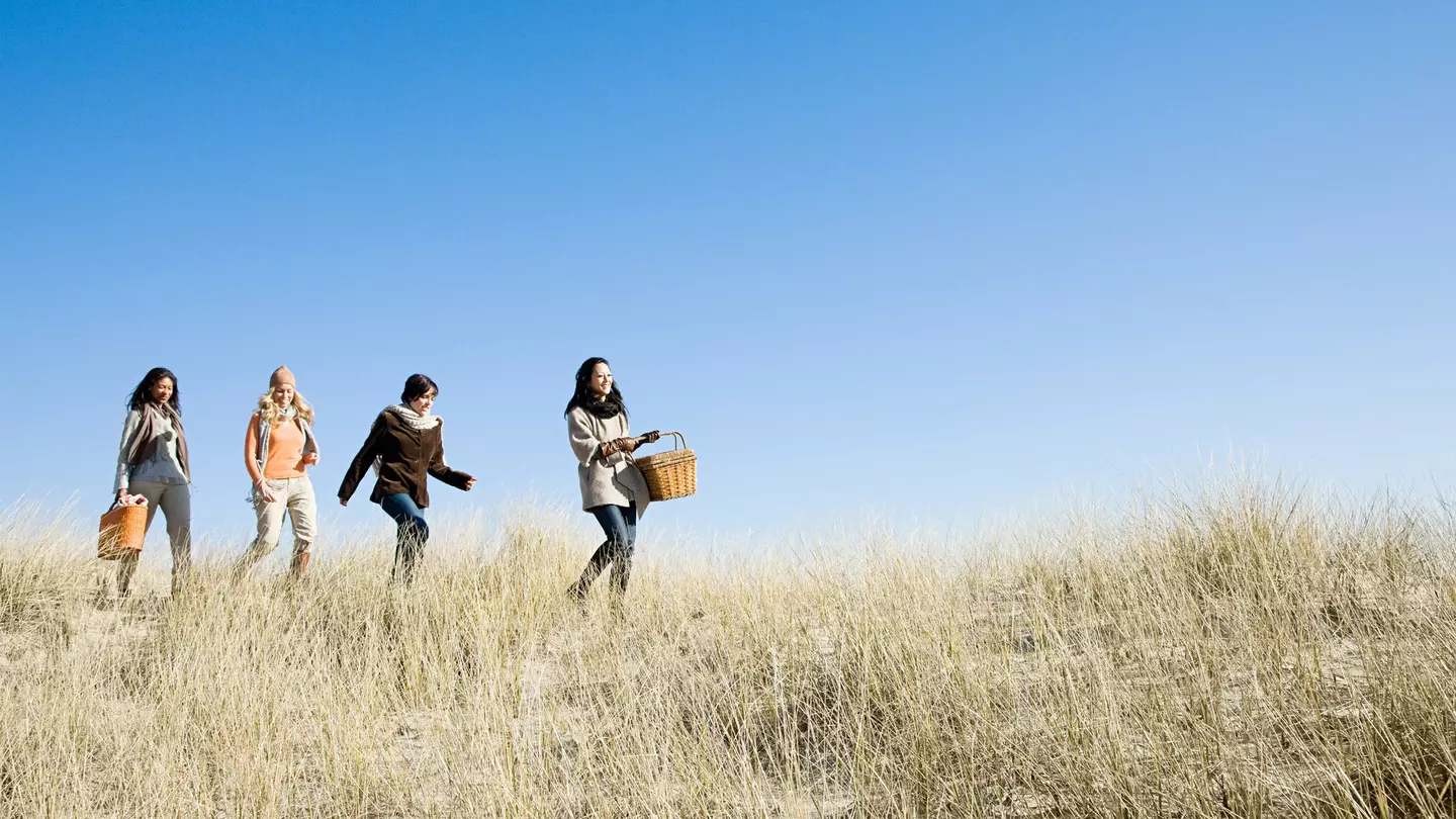 Female friends wearing coats and scarves, walking in marram grass on a sunny day in Cape Cod