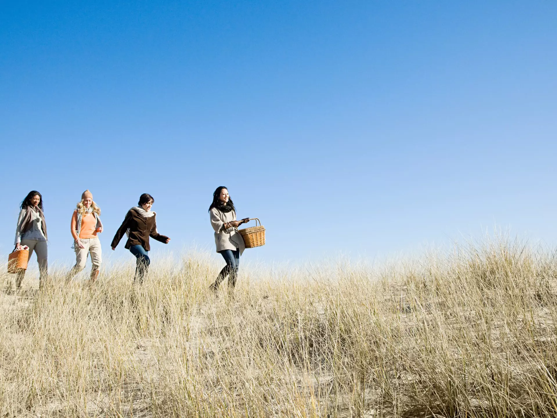 Female friends wearing coats and scarves, walking in marram grass on a sunny day in Cape Cod