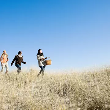 Female friends wearing coats and scarves, walking in marram grass on a sunny day in Cape Cod