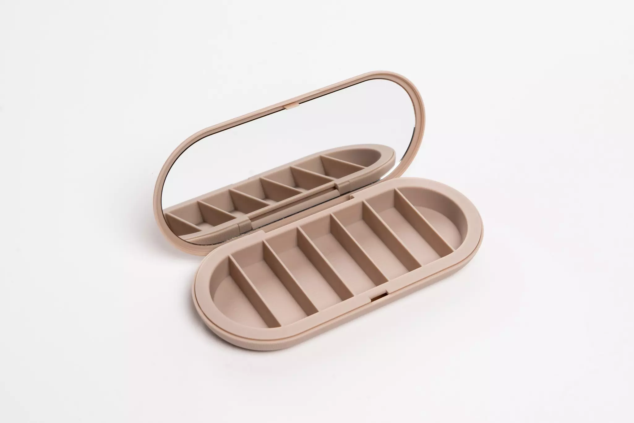 A tan oval-shaped container with seven compartments and a mirror.