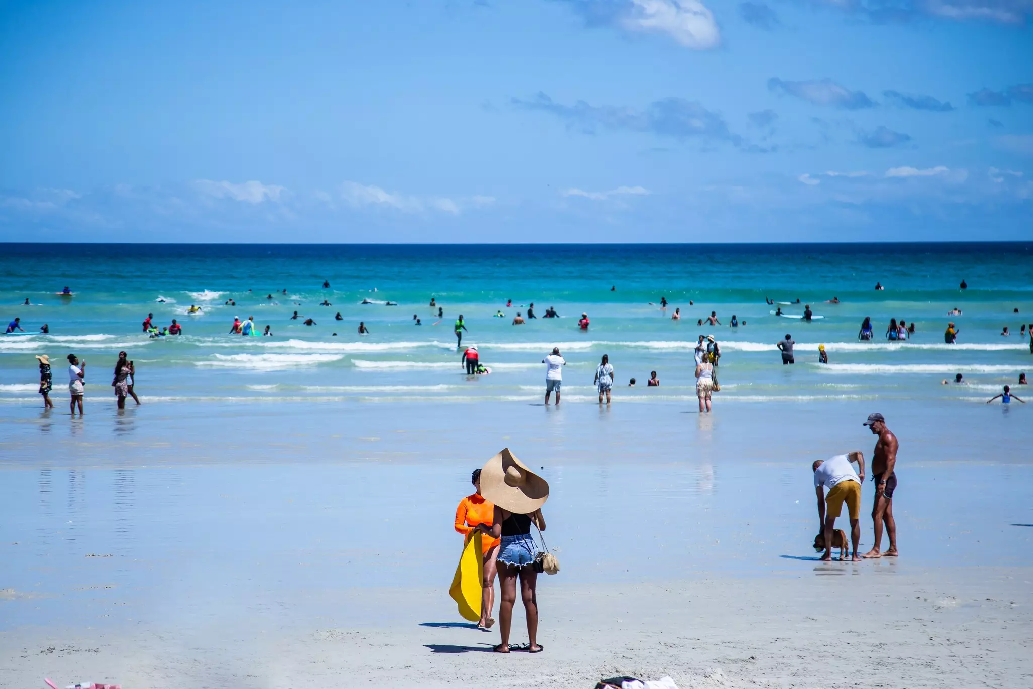 Numbers of people are pictured on a beach and in the ocean on a beautiful day.