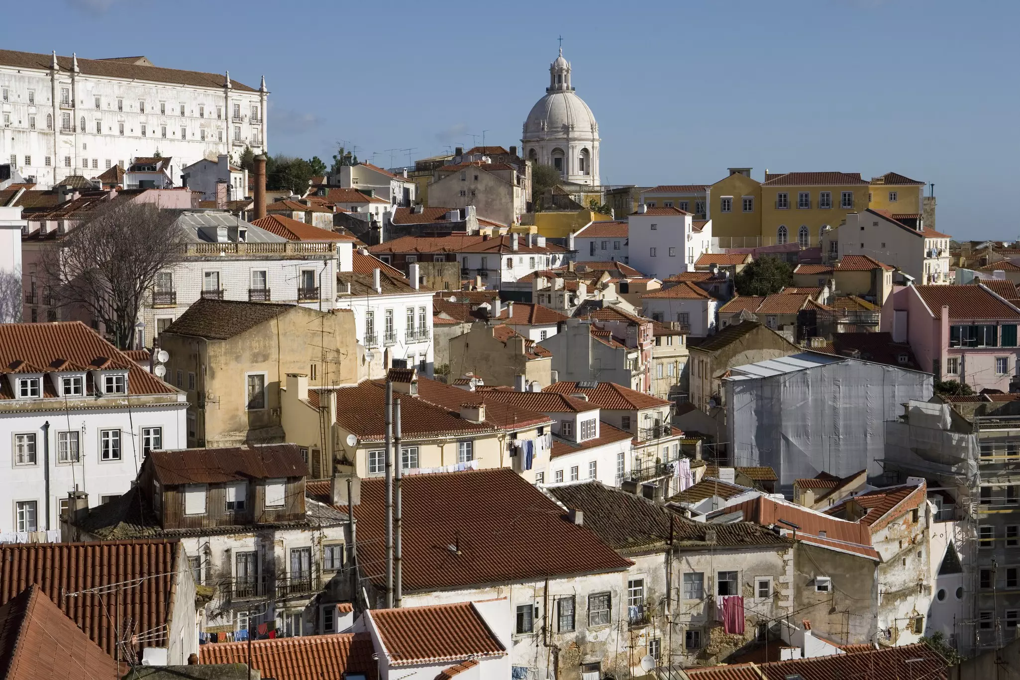 Red-tiled roofs of historic buildings on a hill in a city are pictured from a viewpoint above. A large cupola is seen in the distance.