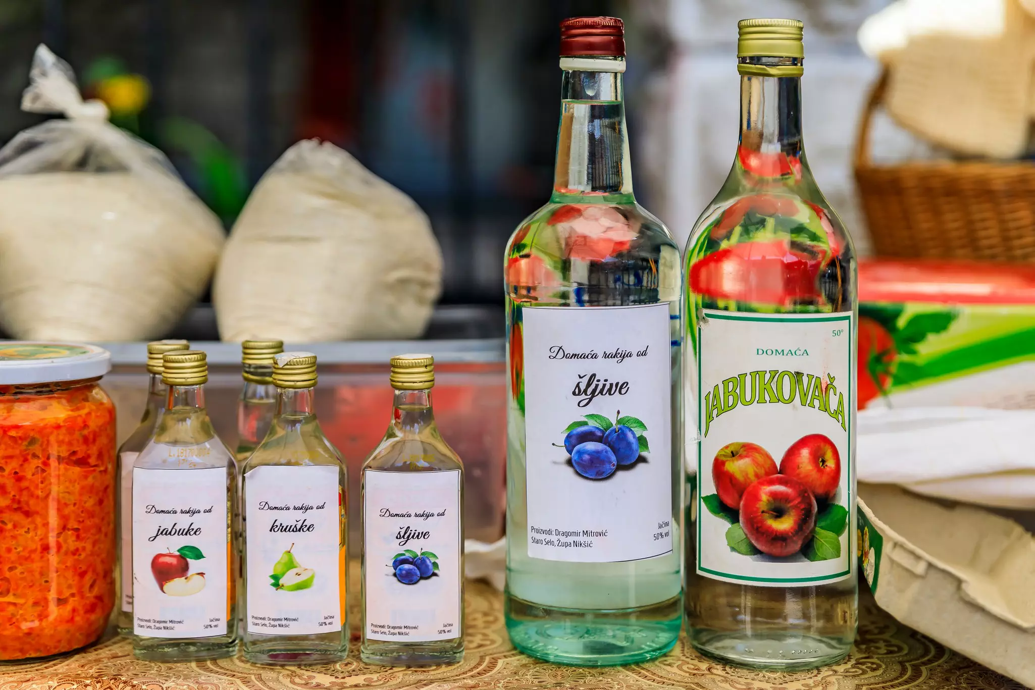 Two large bottles and five small bottles of clear liquid with homemade labels with fruit illustrations.