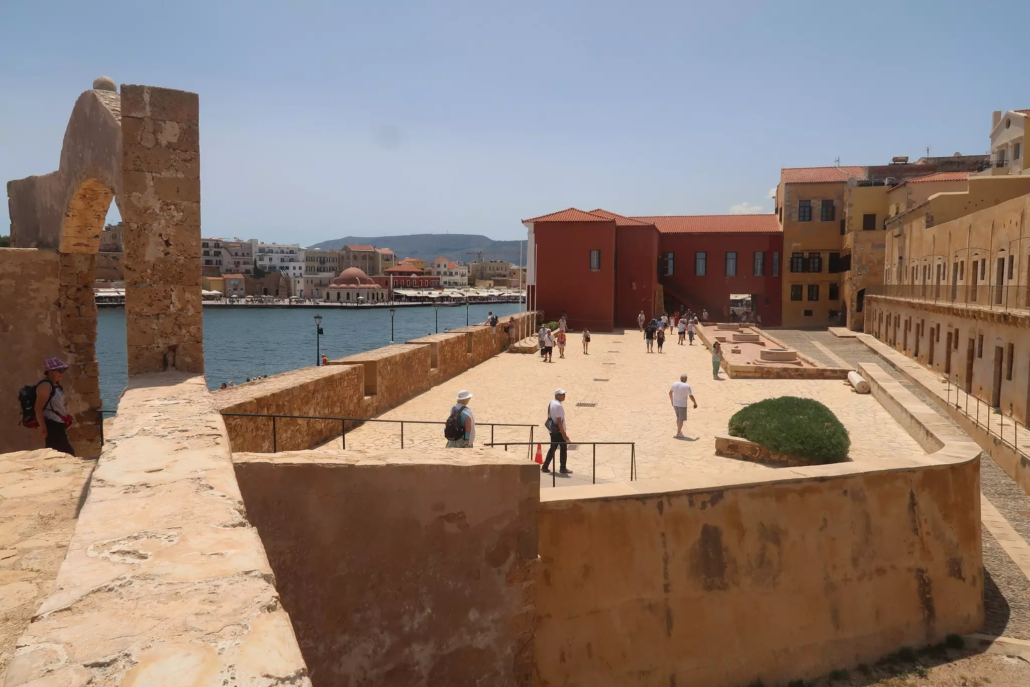 A wide view of people walking on top of a historic fortification by a city harbor.