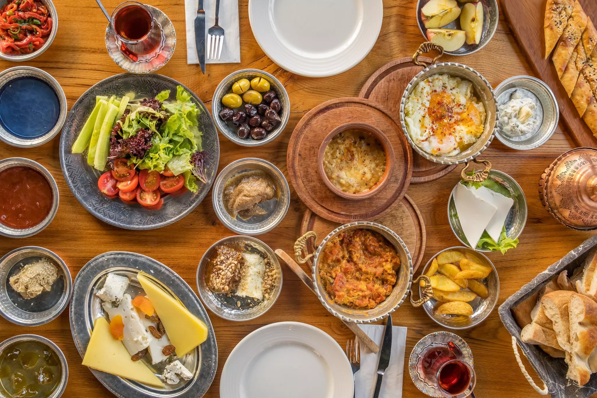 An overhead view of a table filled with dishes containing eggs, bread, cheese, stews and other foods.