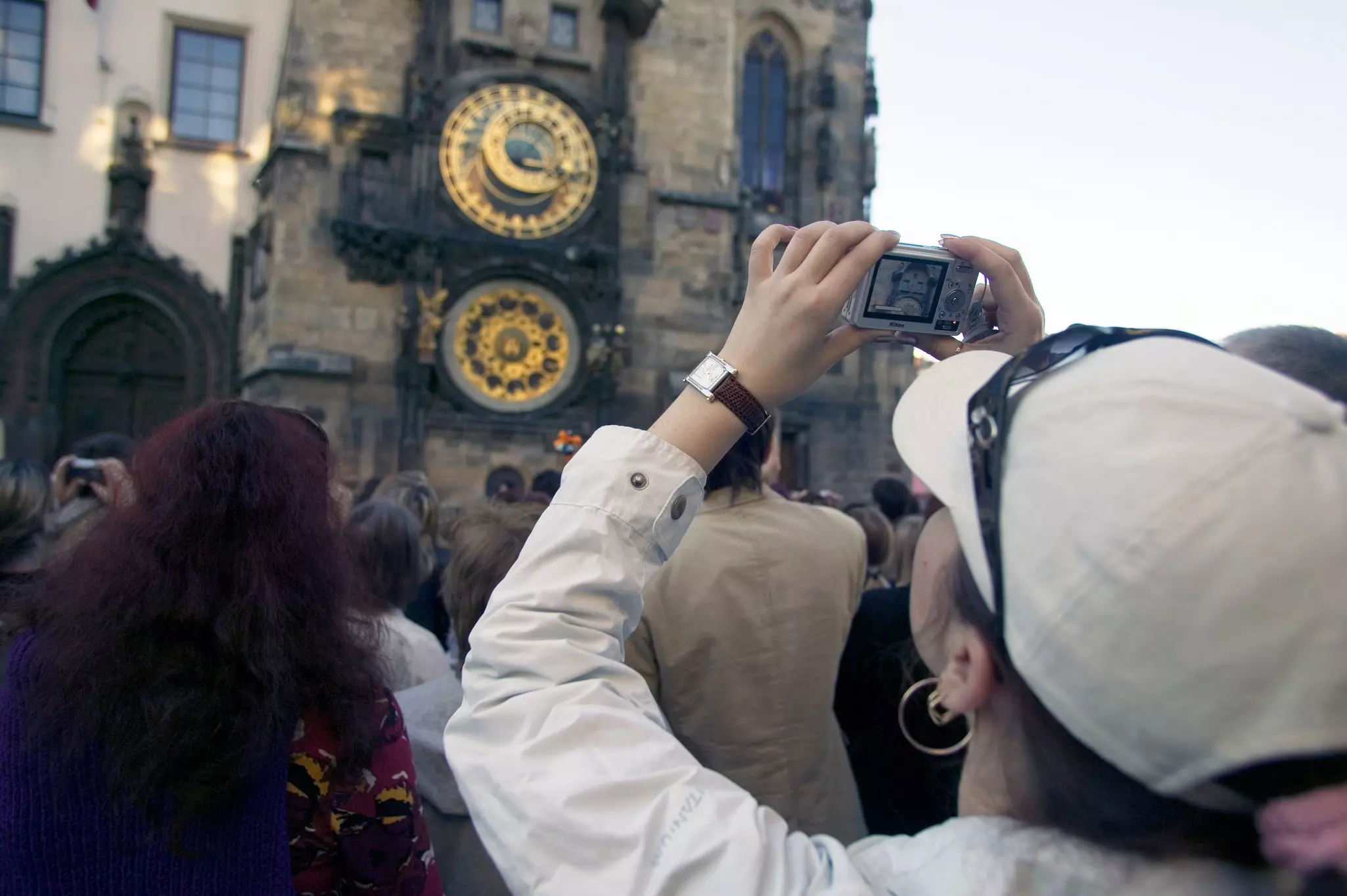A woman with a digital camera holds it up over a crowd toward an old clock