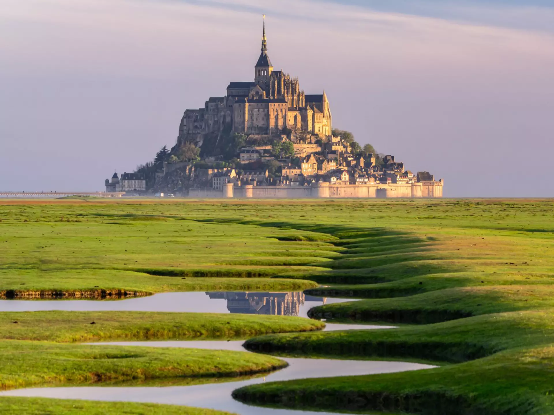 A river curves through green grass with a cathedral on a hill at the end.